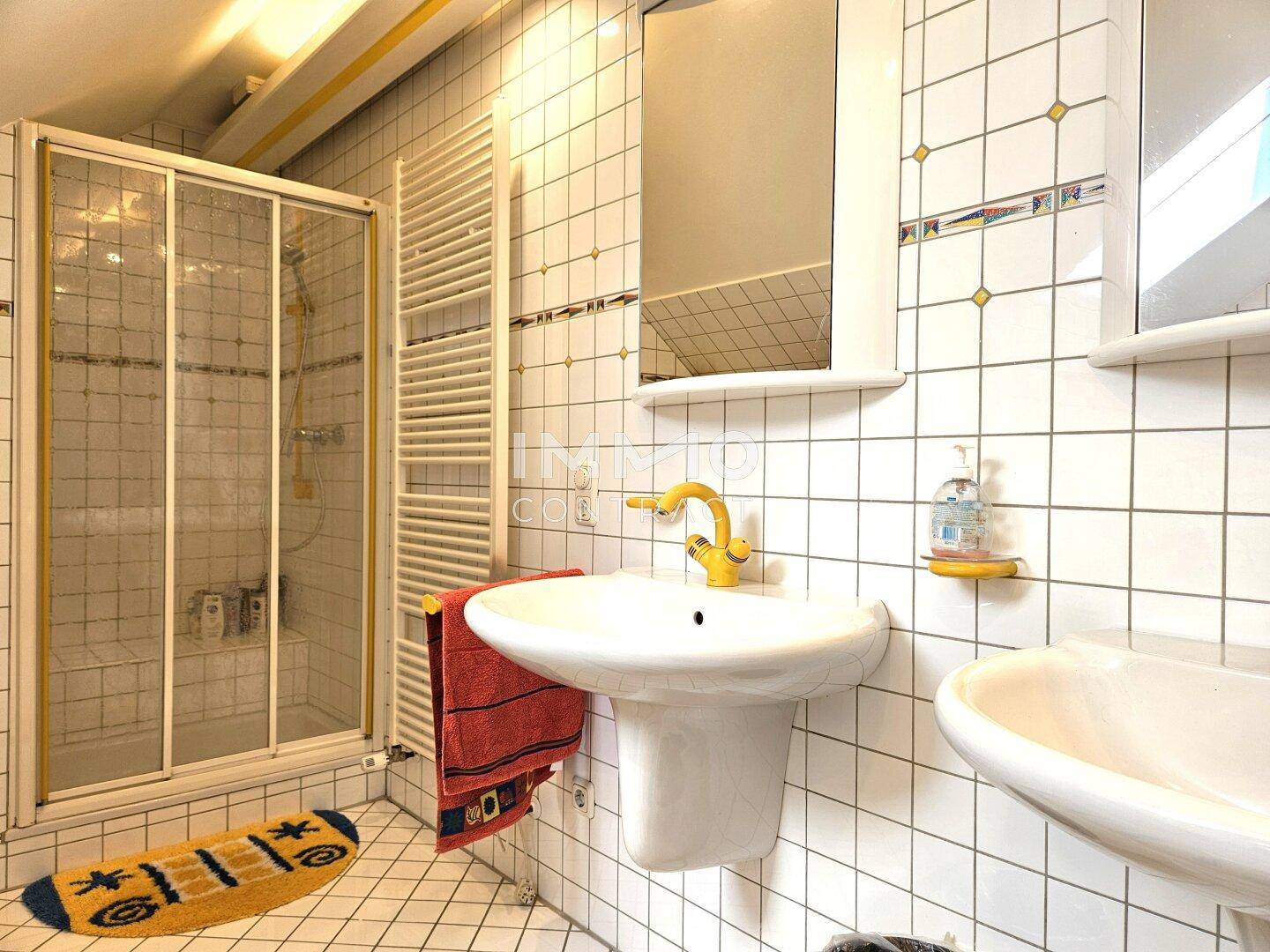 Badezimmer mit Dusche, Waschbecken und weiß-gelben Fliesen.