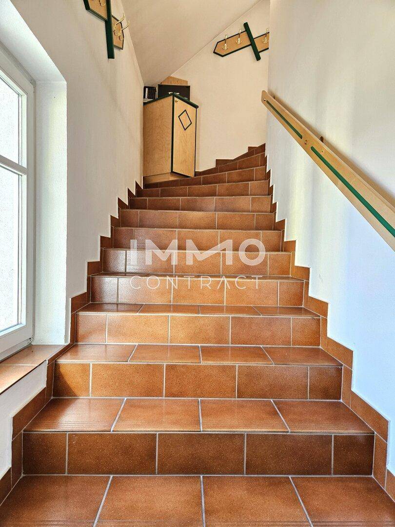 Treppenhaus mit Terrakotta-Fliesen und Holzgeländer, das die Etagen verbindet.