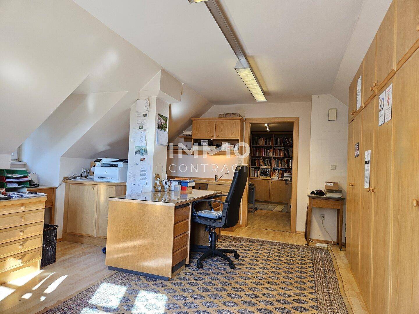 Dachgeschoss-Büro mit Schreibtisch, Einbauschränken und Zugang zu weiteren Räumen.