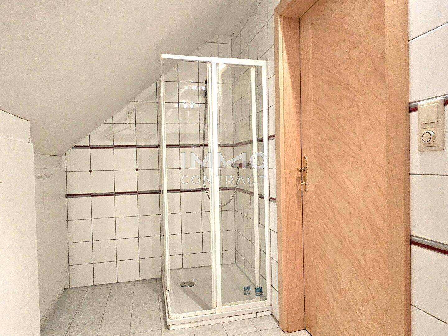Badezimmer im Dachgeschoss mit Duschkabine und weißen Fliesen.