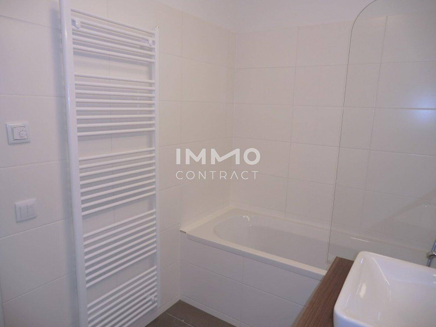 Modernes Badezimmer mit weißen Fliesen, Badewanne, Waschbecken und beheiztem Handtuchhalter.
