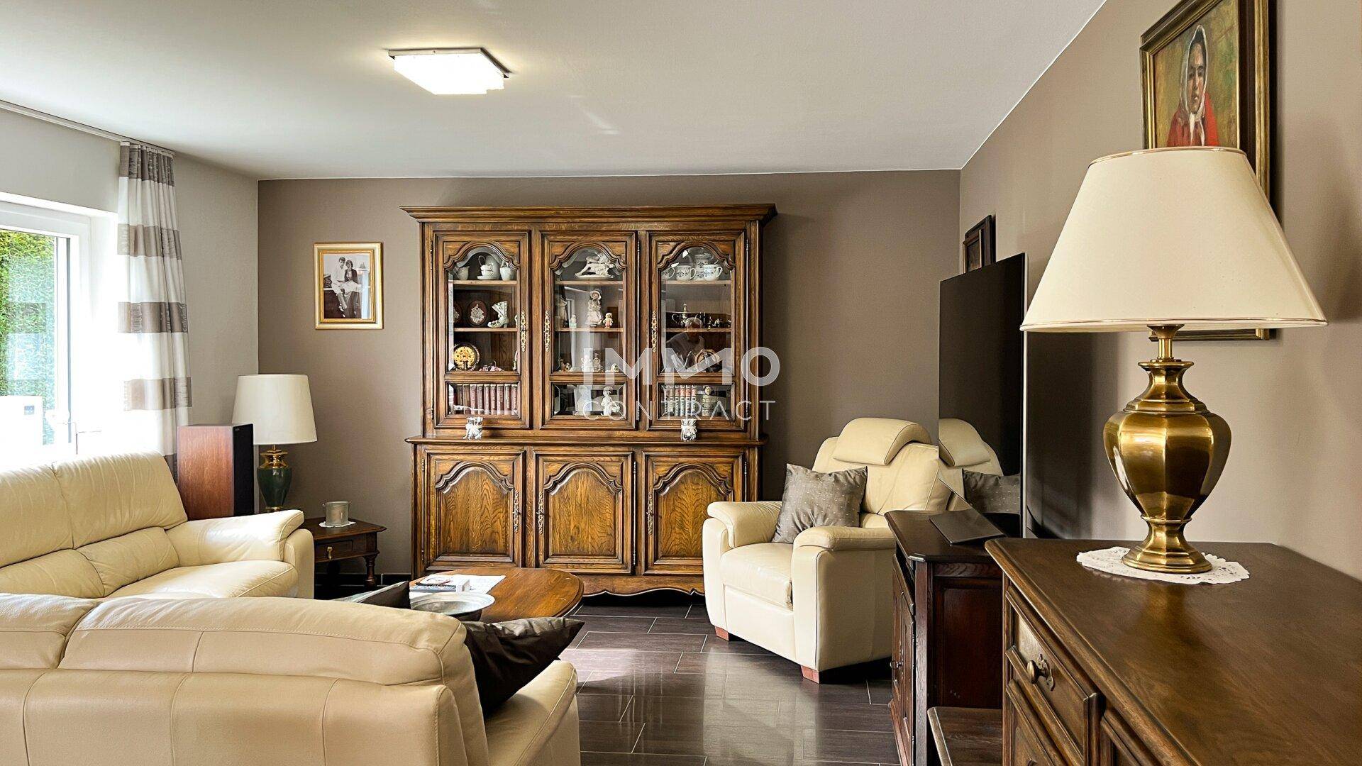 Gemütliches Wohnzimmer mit traditionellen Holzmöbeln, beigen Sofas und dunklem Fliesenboden.