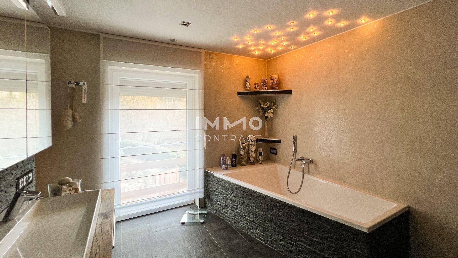 Modernes Badezimmer mit Badewanne, Doppelwaschbecken und indirekter Deckenbeleuchtung.