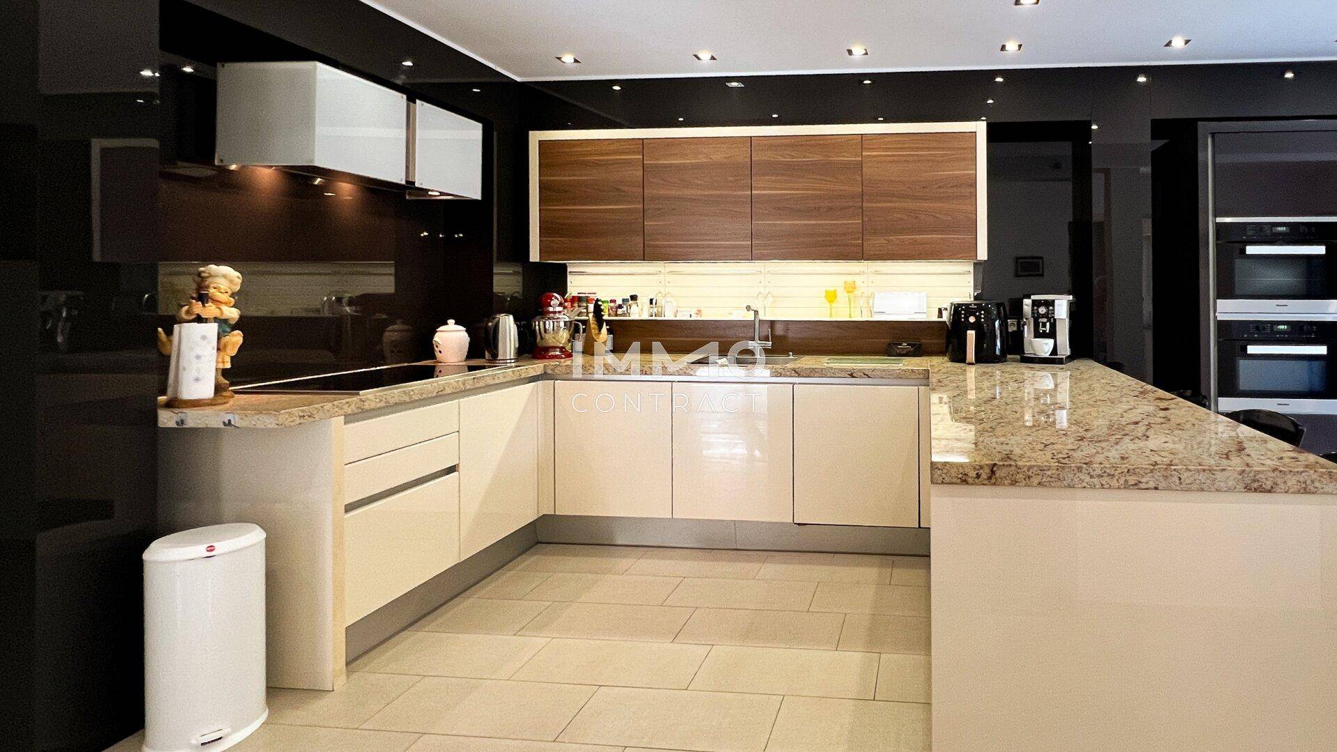 Moderne Küche mit beigen Hochglanzfronten, Granitarbeitsplatten und integrierten Geräten.