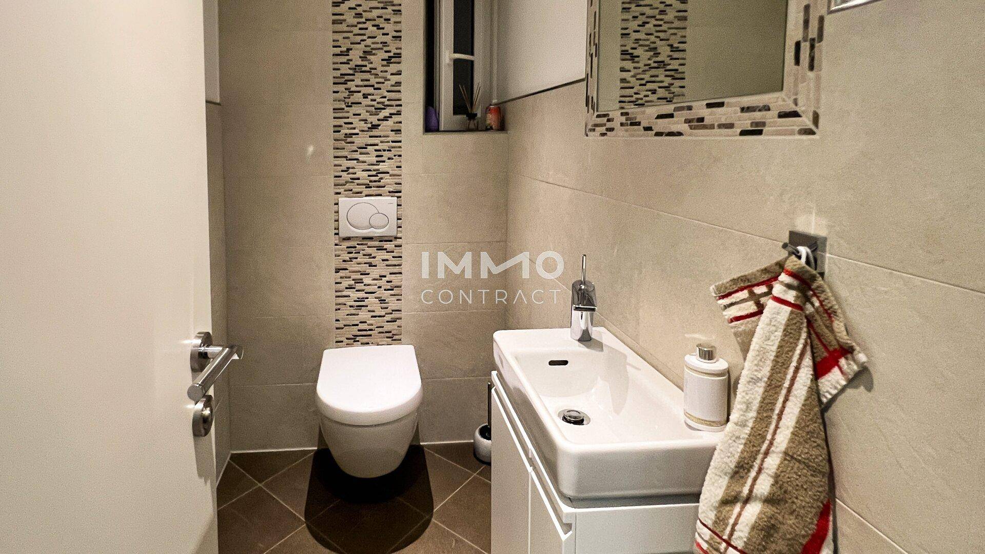 Gäste-WC mit wandhängender Toilette, kleinem Waschbecken und modernen Fliesen.