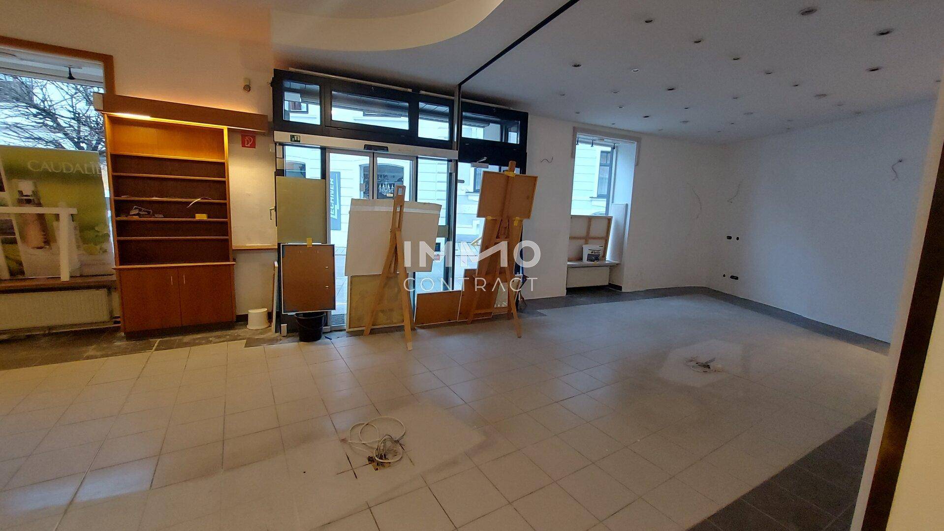 Weitläufiger Gewerberaum mit großen Schaufenstern, Fliesenboden und viel Tageslicht.