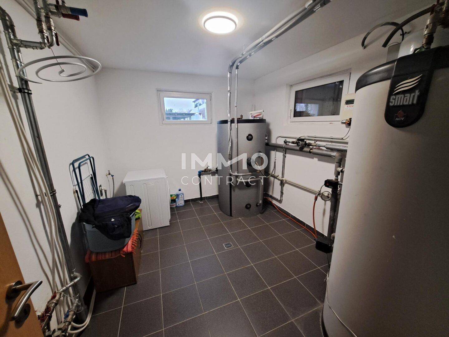 Hauswirtschaftsraum im Keller mit Warmwasserspeichern, Waschmaschine und Fenster.