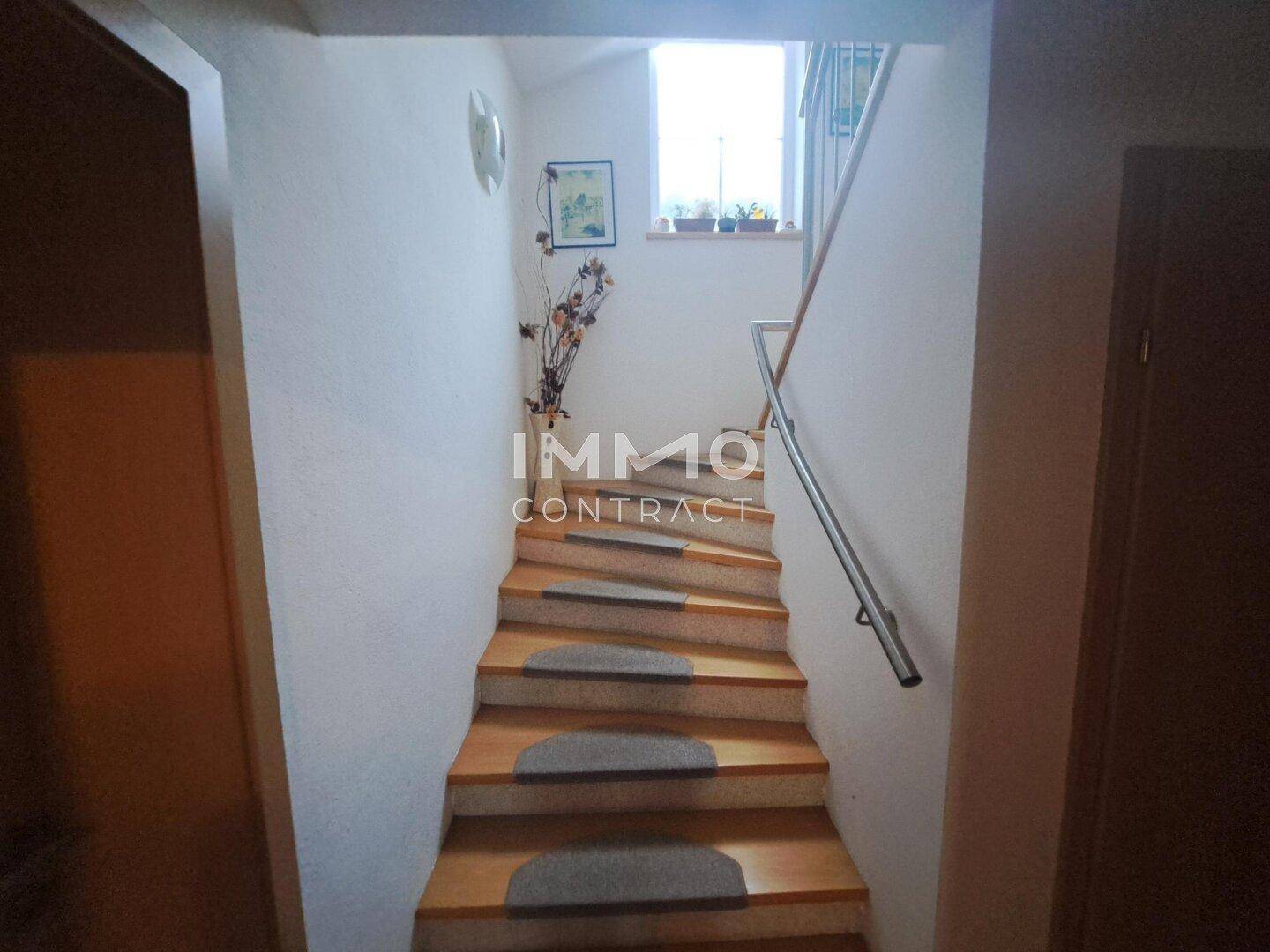 Holztreppe mit Teppichstufen und Fenster, die zu den oberen Etagen führt.