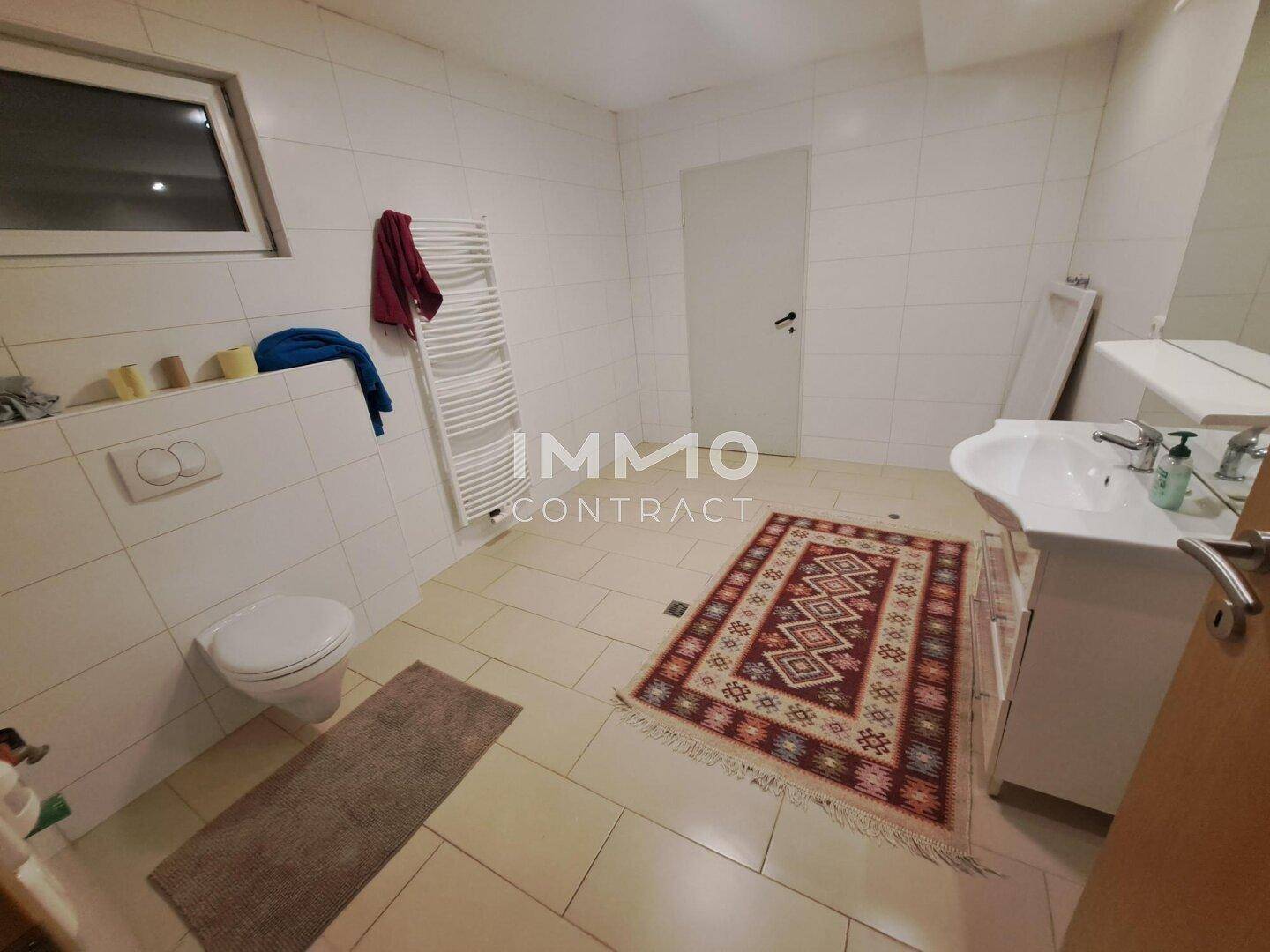 Modernes Badezimmer mit WC, Waschbecken, Fenster und Handtuchheizkörper.