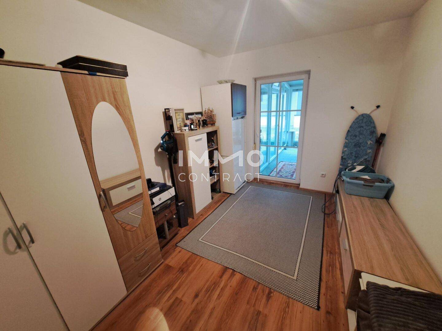 Schlafzimmer mit Laminatboden, Kleiderschrank und Zugang zu einem Wintergarten.