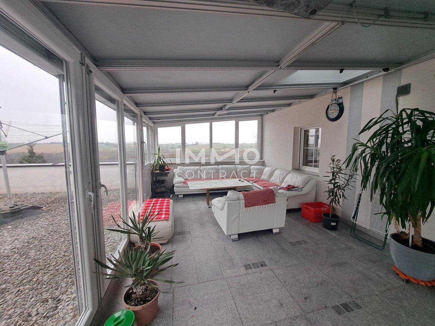 Heller Wintergarten mit Sitzgelegenheiten, Pflanzen und Blick ins Grüne.