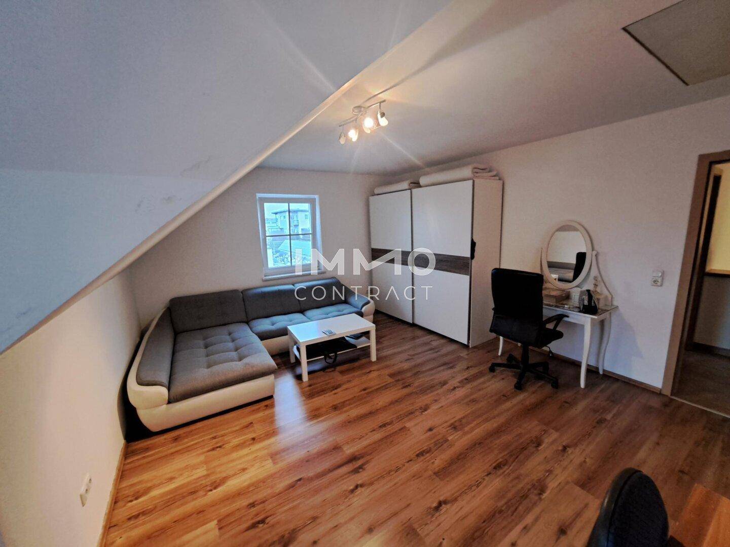 Dachgeschosszimmer mit Sofa, Schreibtisch und Laminatboden unter der Dachschräge.