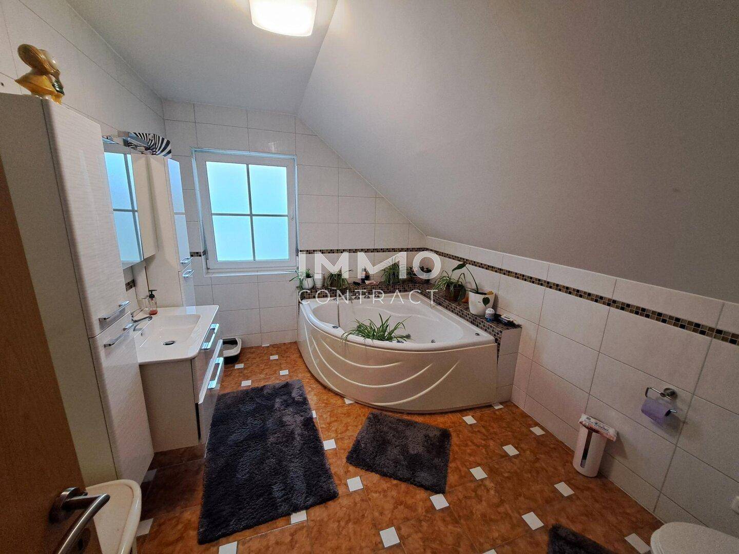 Badezimmer im Dachgeschoss mit Eckbadewanne, Fenster und Fliesenboden.
