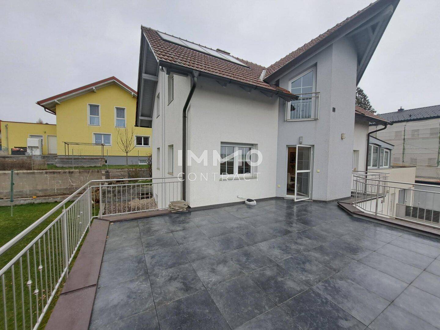 Große Außenterrasse mit dunklen Fliesen und Blick auf den Garten und die Umgebung.