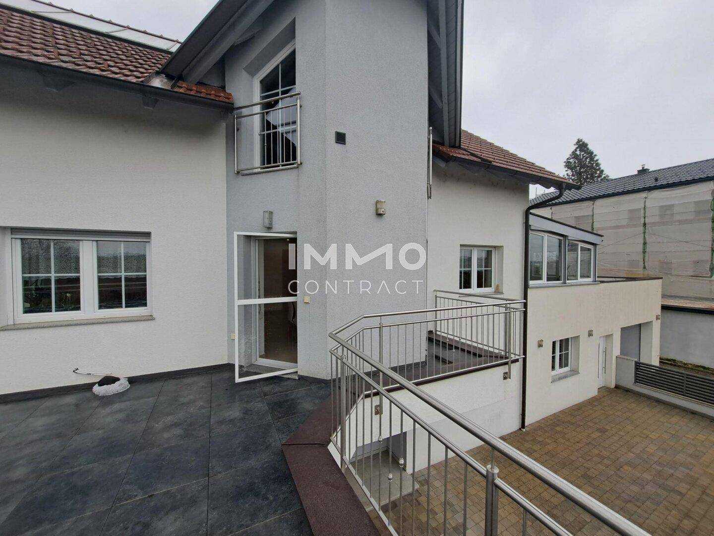Große, geflieste Terrasse mit Metallgeländer und Zugang zum Haus.