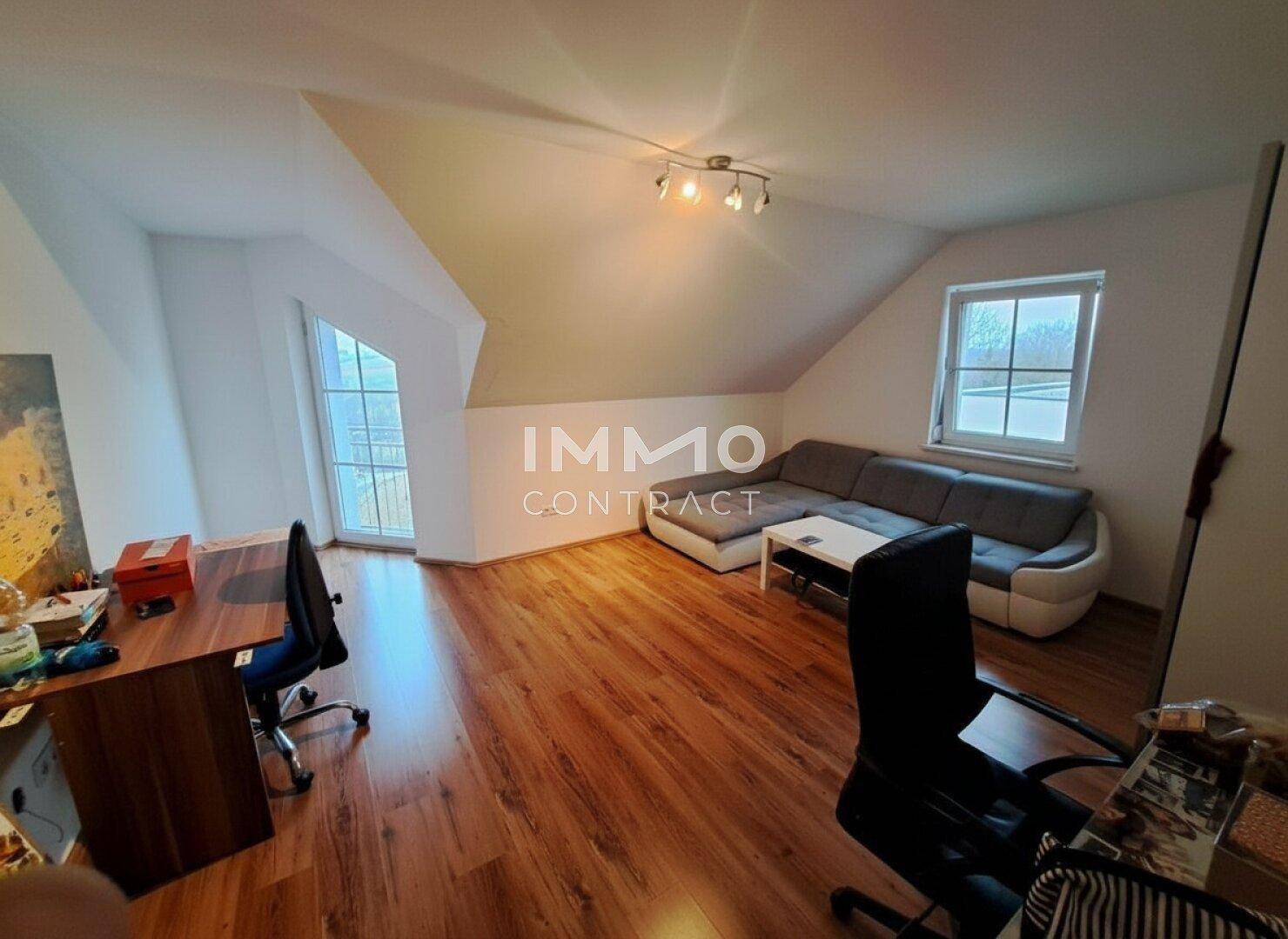 Geräumiges Dachgeschosszimmer mit Sitzbereich, Schreibtisch und Laminatboden.