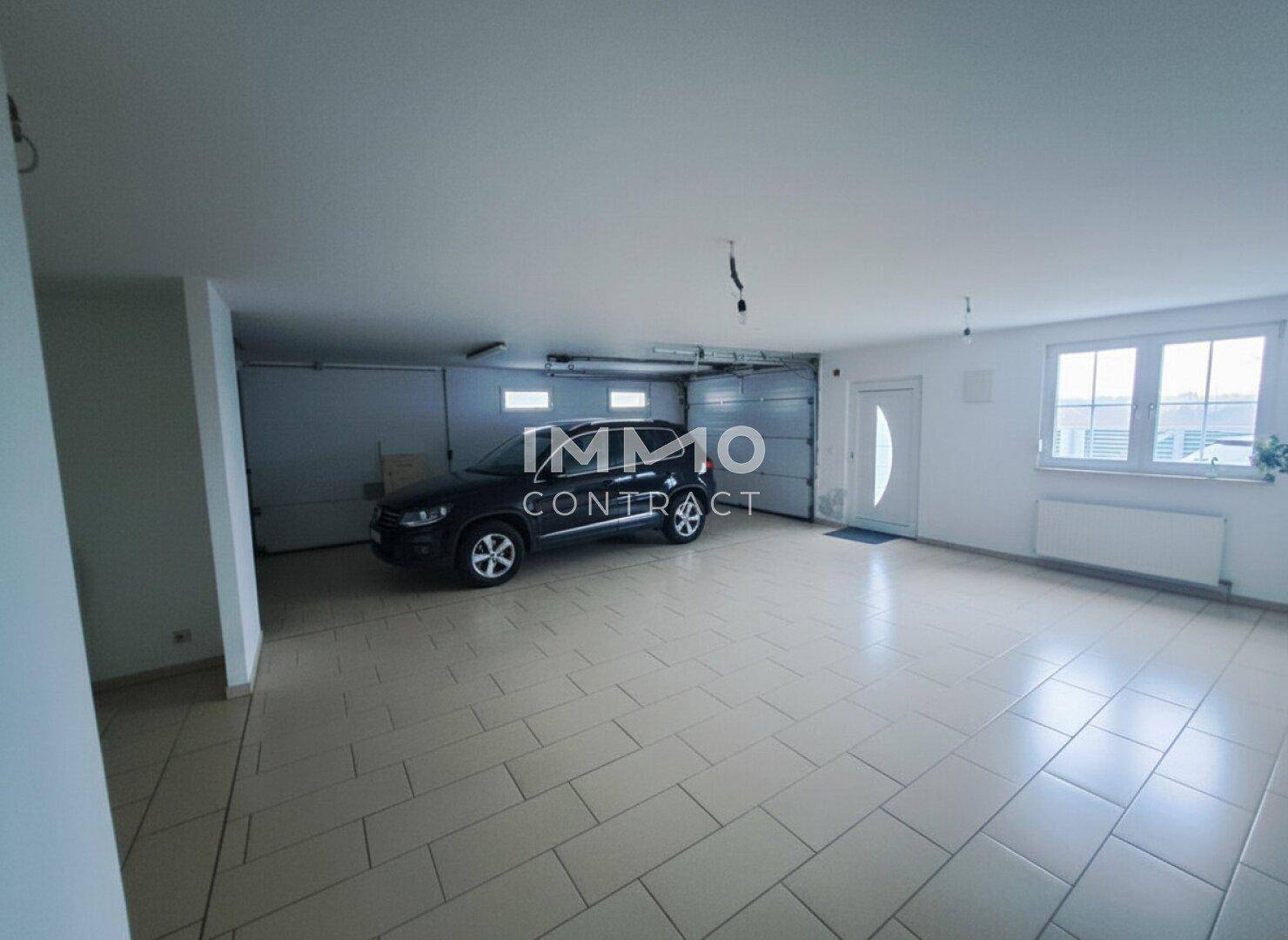 Geräumige Garage mit Fliesenboden, Platz für mehrere Fahrzeuge und Fenstern.