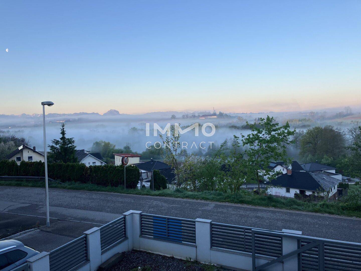 Panoramablick über eine neblige Landschaft mit Häusern und Bergen im Hintergrund.