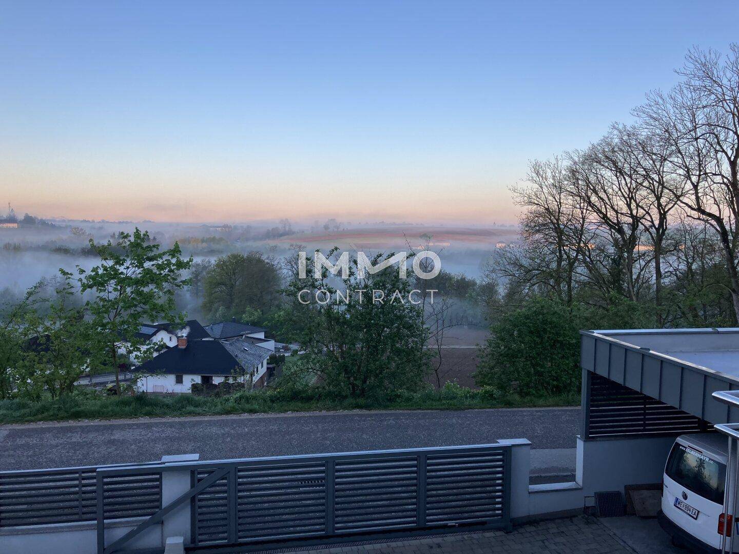Weitläufiger Ausblick über eine ländliche Gegend mit Bäumen und Nebel am Morgen.