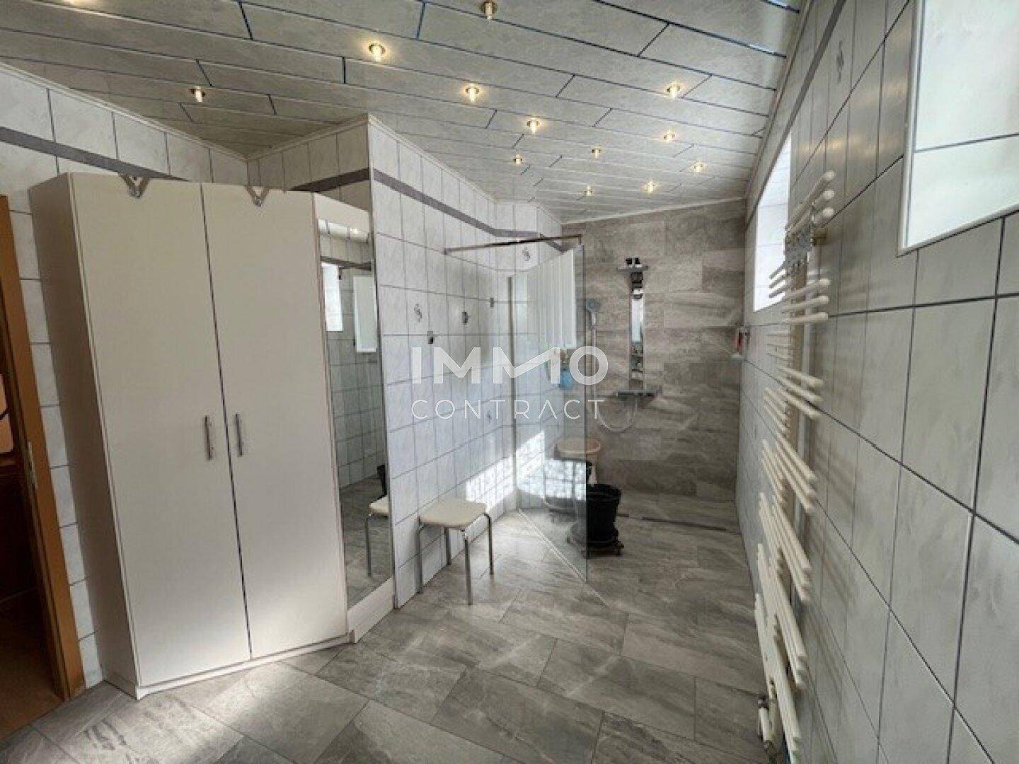 Modern gefliestes Badezimmer mit großer begehbarer Dusche und beheiztem Handtuchhalter.