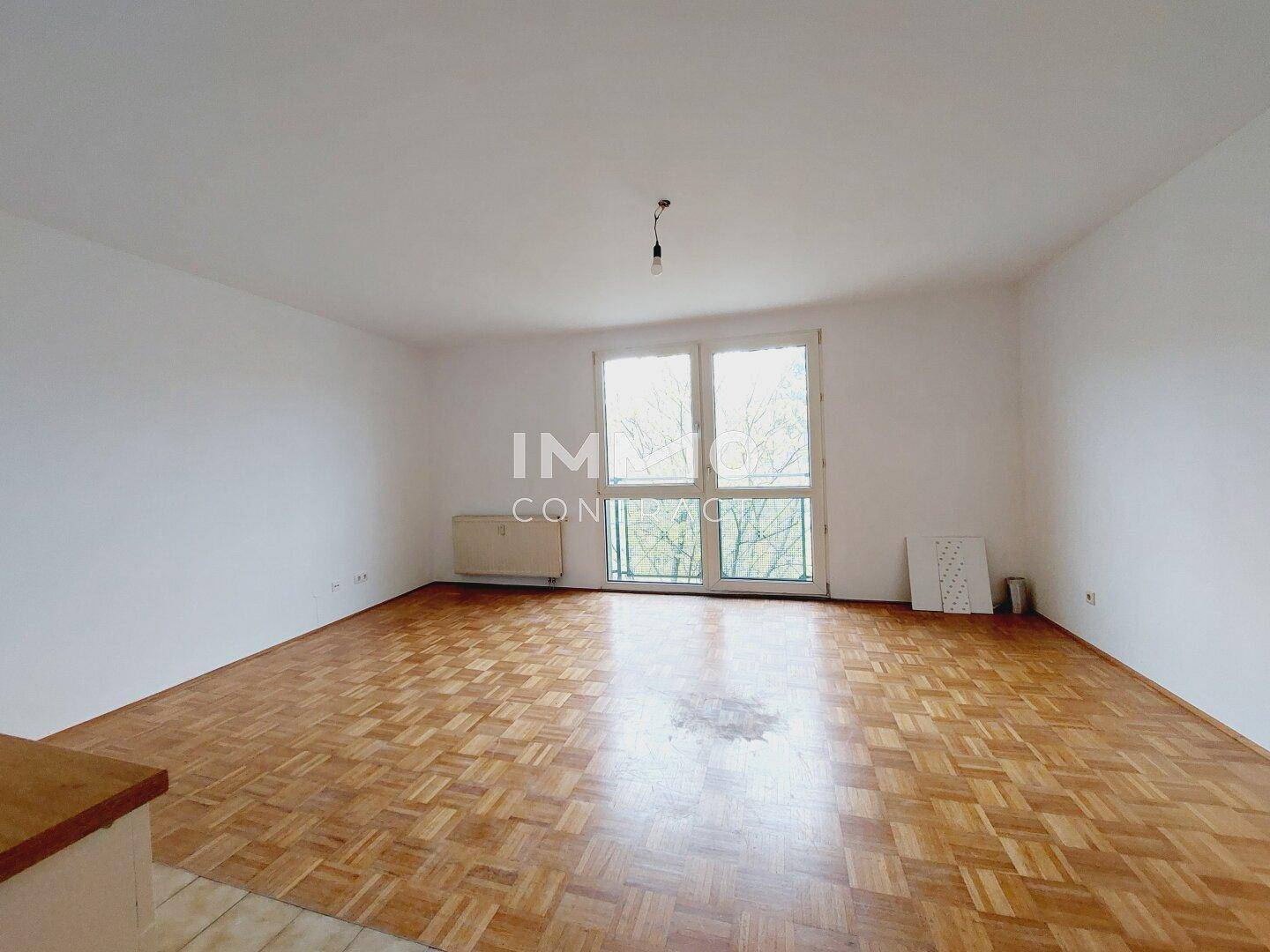 Geräumiges Wohnzimmer mit klassischem Parkettboden und großen Fenstern für viel Tageslicht.