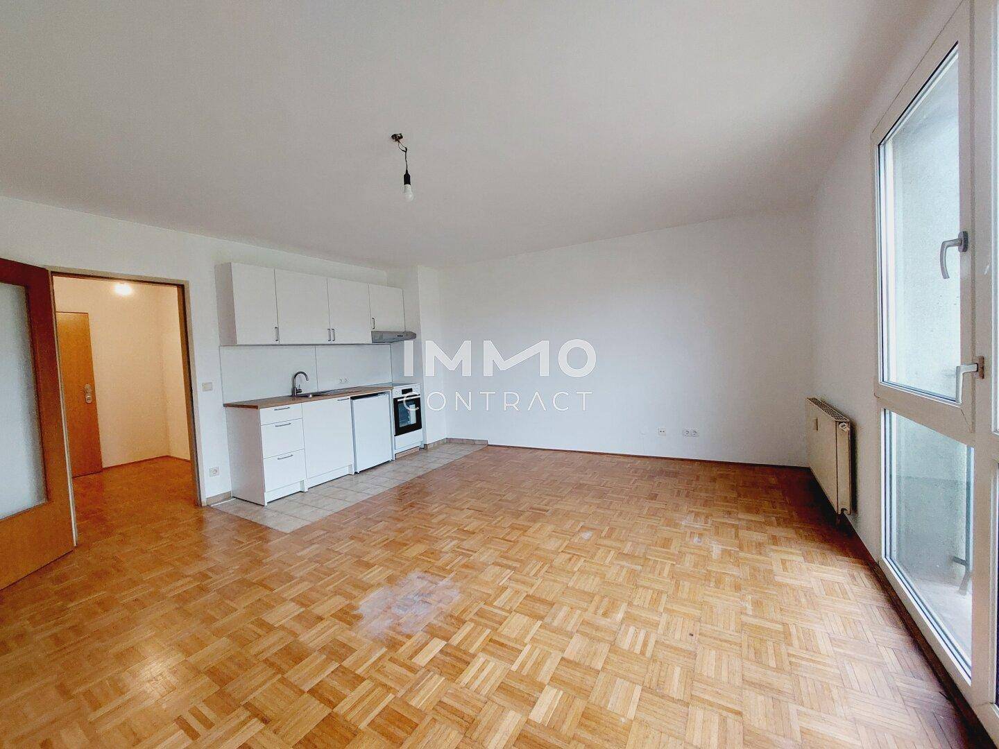 Heller Wohnbereich mit integrierter Küchenzeile, Parkettboden und Zugang zu einem weiteren Raum.