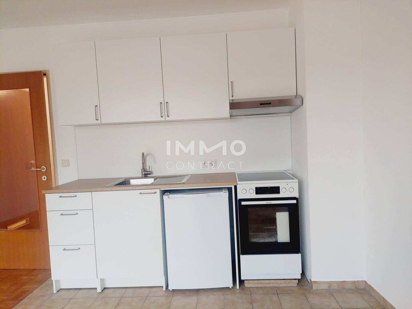 Kompakte Küchenzeile mit weißen Schränken, Spüle, Kühlschrank und Herd.