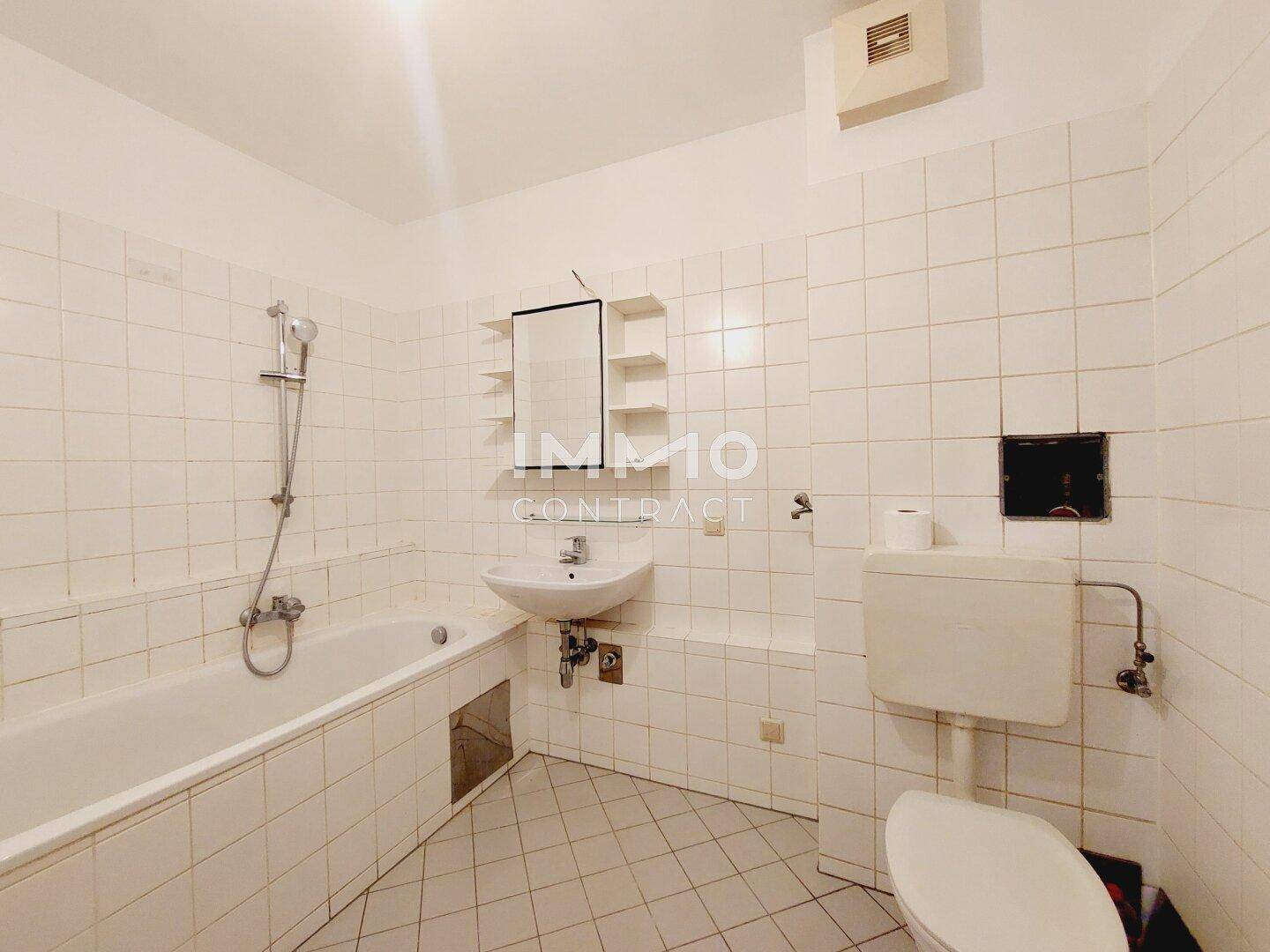 Badezimmer mit Badewanne, WC, Waschbecken und weißen Fliesen im 80er-Jahre-Stil.