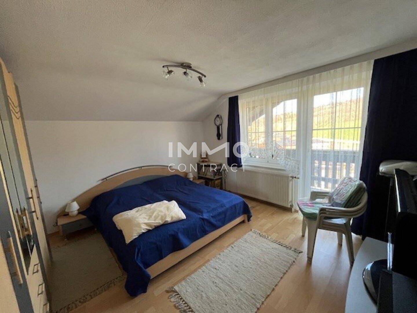 Helles Schlafzimmer mit Holzboden, Dachschräge und Zugang zu einem kleinen Balkon mit Weitblick.