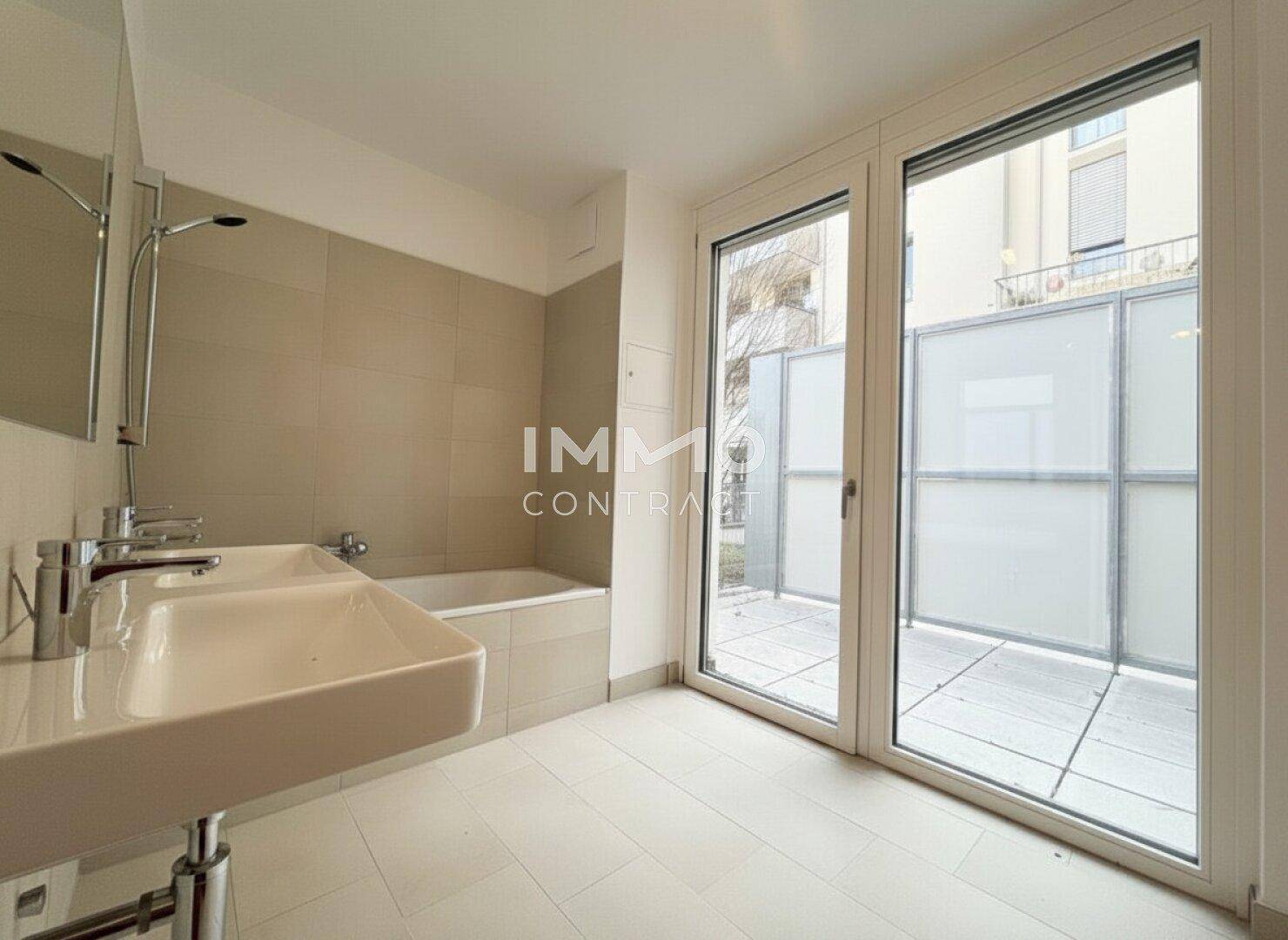 Modernes Badezimmer mit Doppelwaschbecken, Badewanne und Zugang zu einer kleinen Außenterrasse.