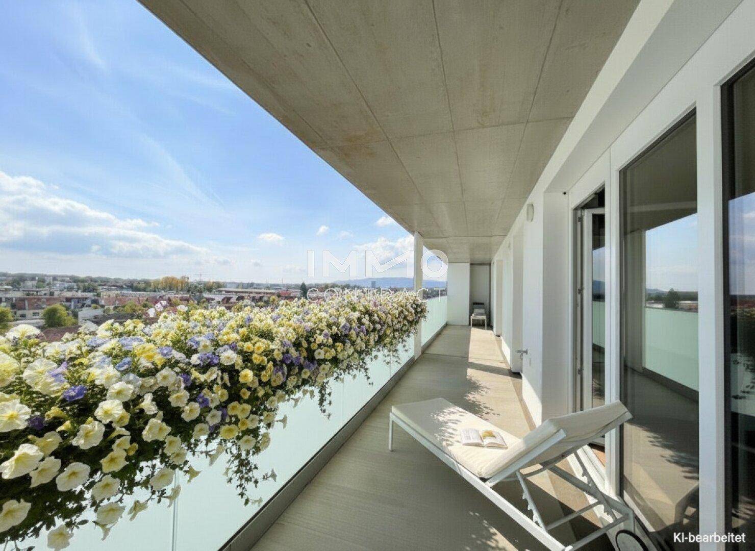 Langer Balkon mit bunten Blumenkästen, Liegestuhl und weitem Blick über die Stadtlandschaft.