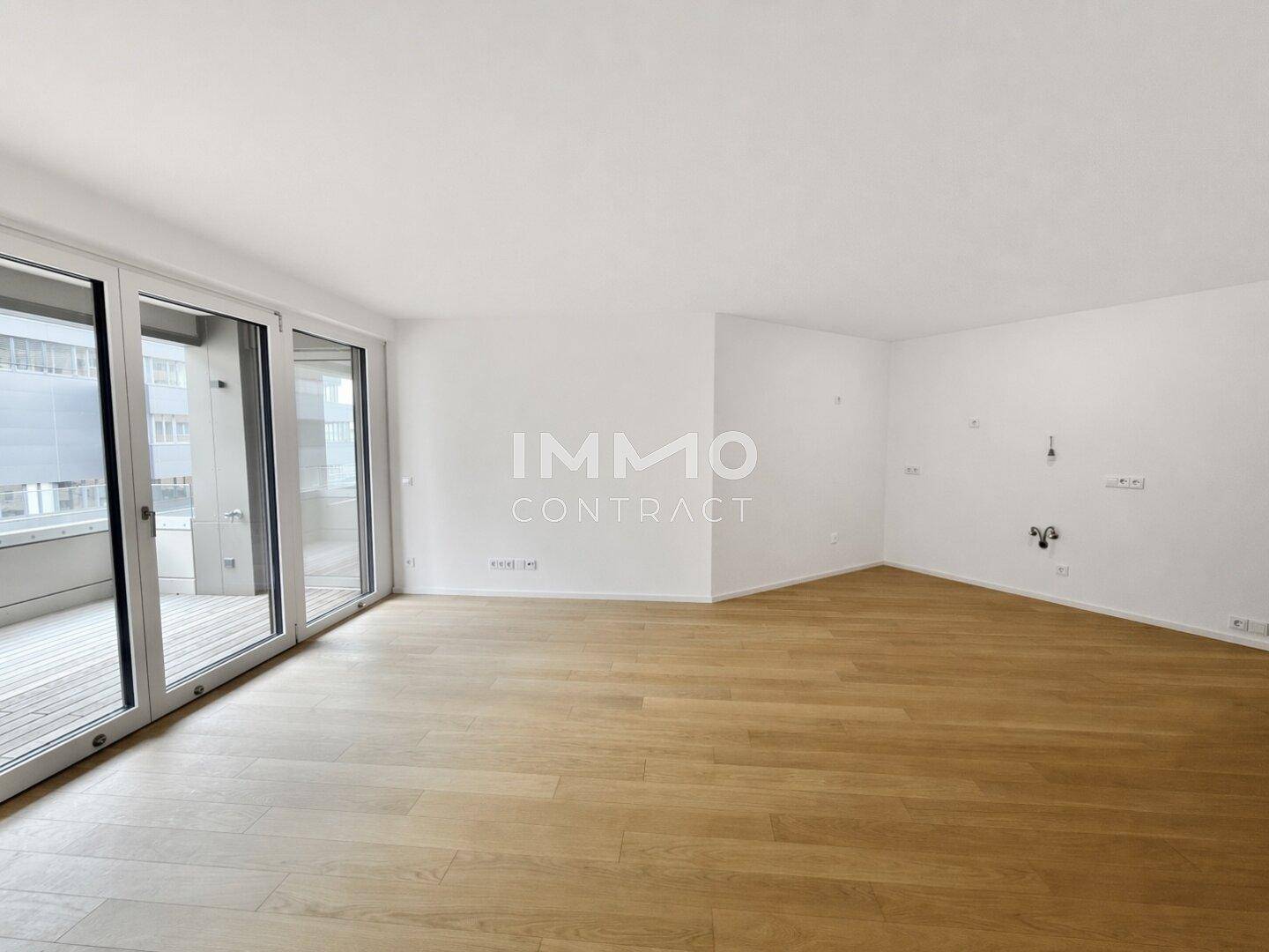 Geräumiges Wohnzimmer mit hellem Parkettboden und großen Fenstern zum Balkon.