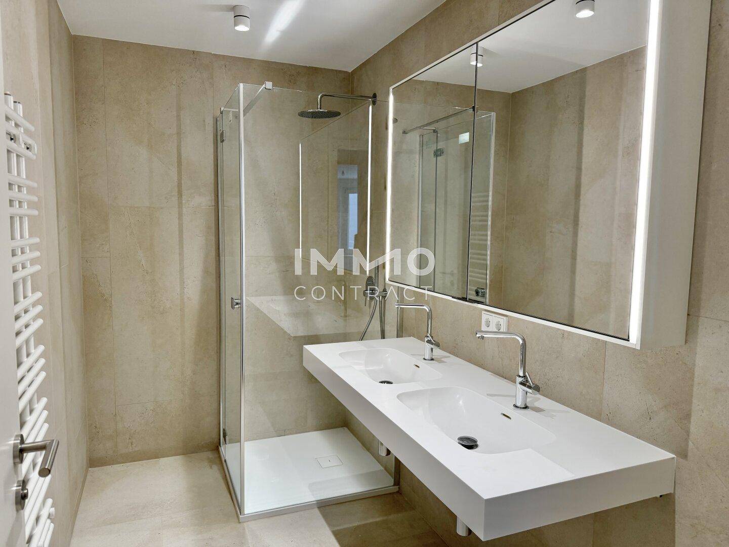 Modernes Badezimmer mit Doppelwaschbecken, großer Dusche und beigen Fliesen.