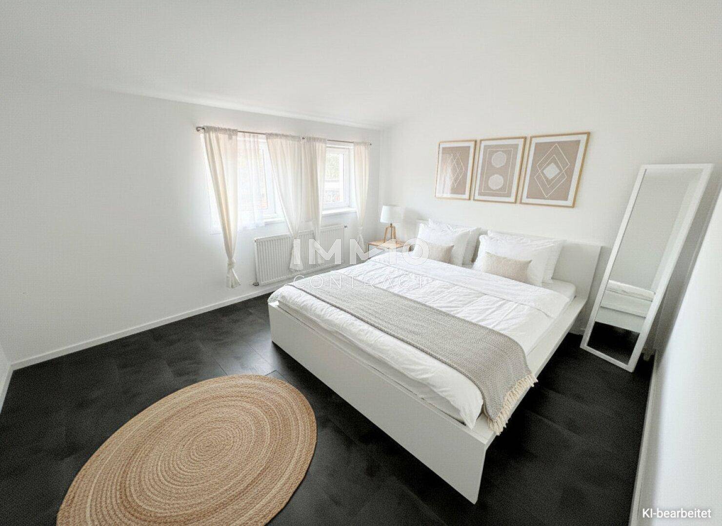 Helles Schlafzimmer mit dunklem Boden, einem großen Bett und modernen Bildern an der Wand.