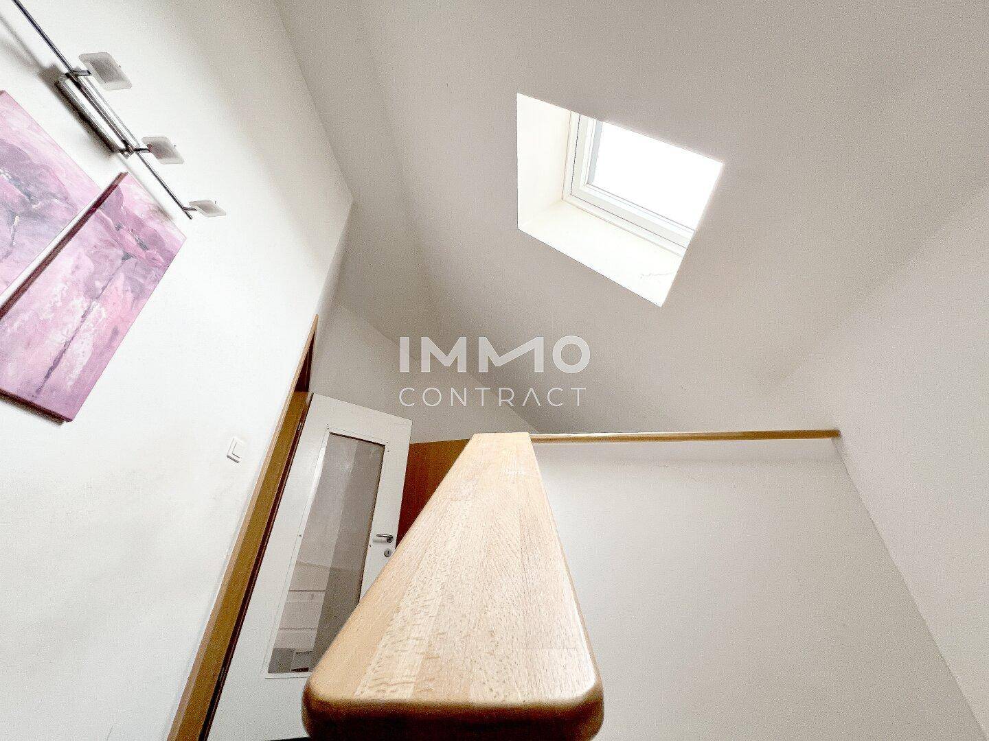 Heller Treppenaufgang mit Holzgeländer und einem Dachfenster, das viel natürliches Licht spendet.