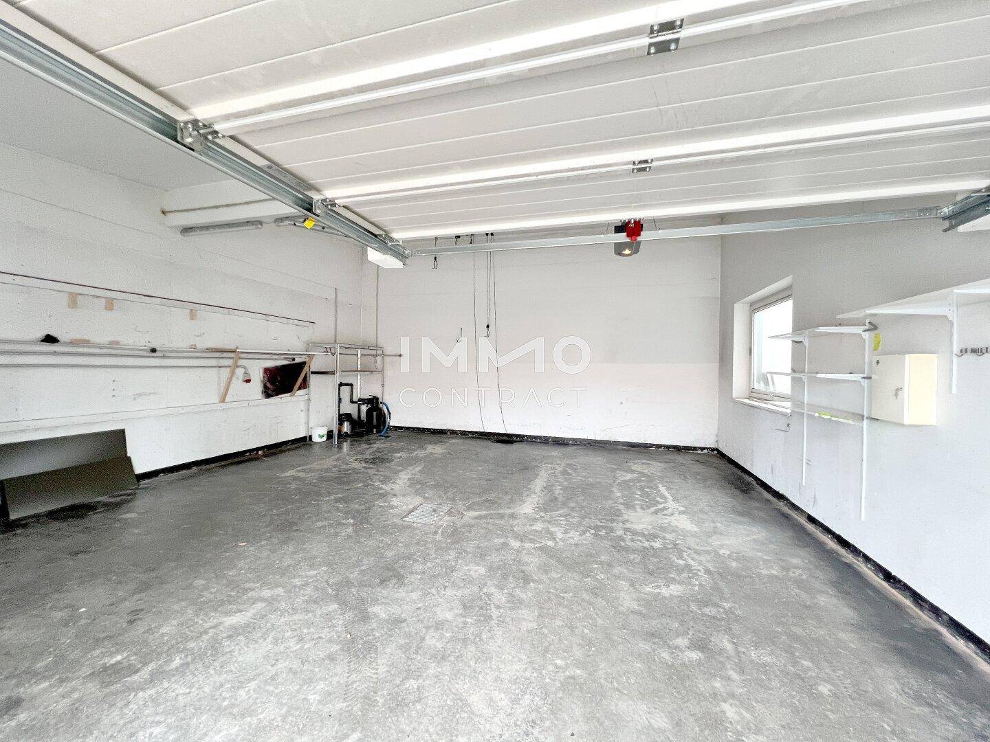 Geräumige Garage mit Betonboden und einem Fenster, bietet Platz für Fahrzeuge und Lagerung.