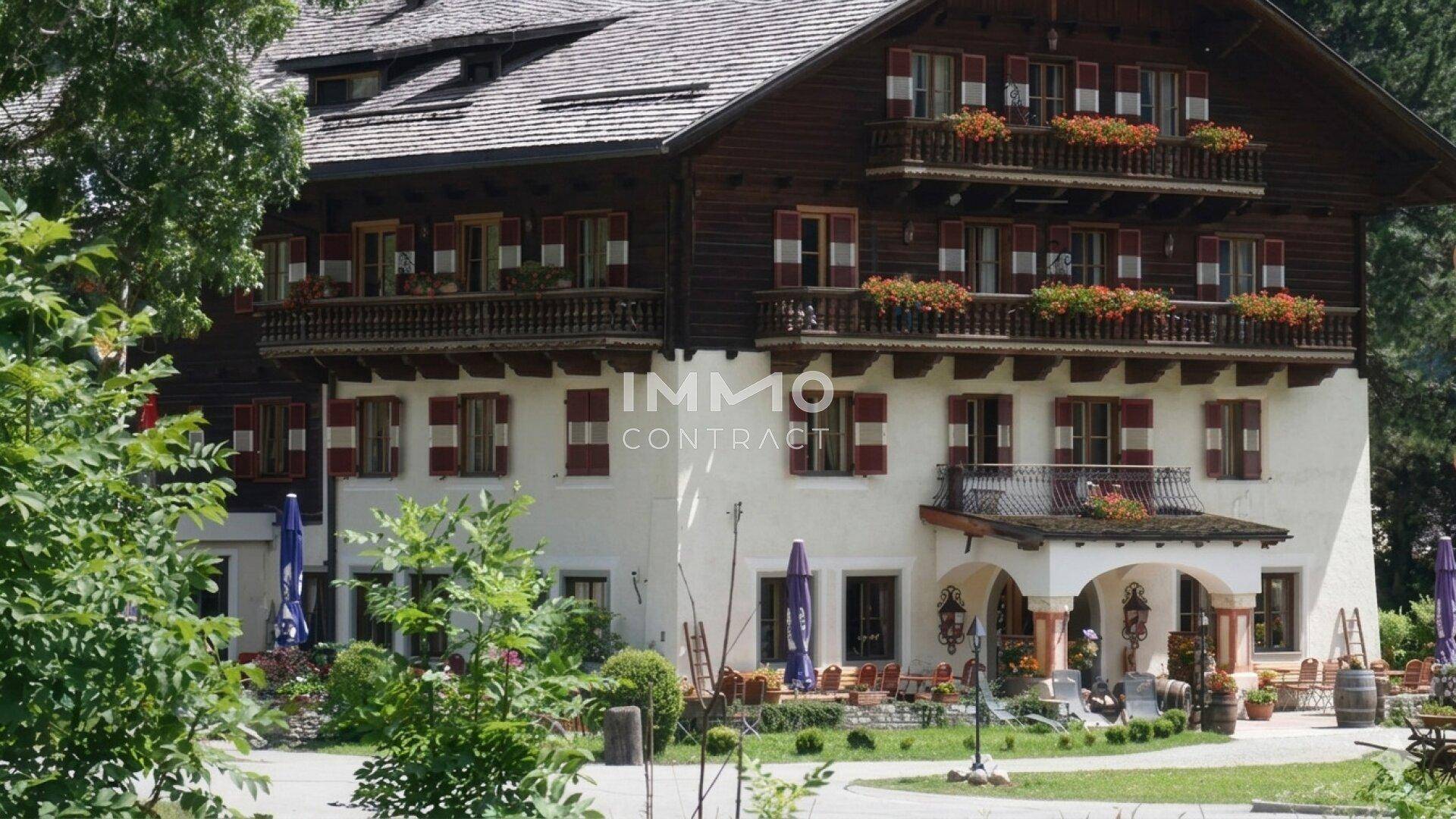 Traditionelles Gebäude mit Holzbalkonen, roten Fensterläden und blühenden Blumenkästen in alpiner Umgebung.