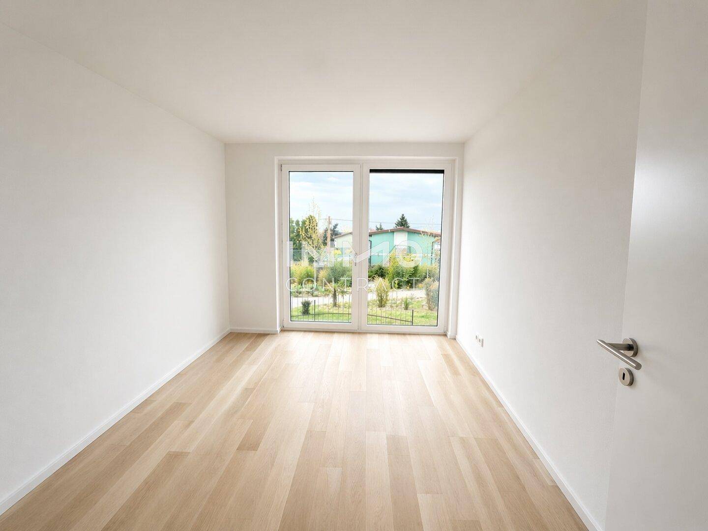 Helles Zimmer mit Holzboden und großen Fenstern, die viel Tageslicht hereinlassen.