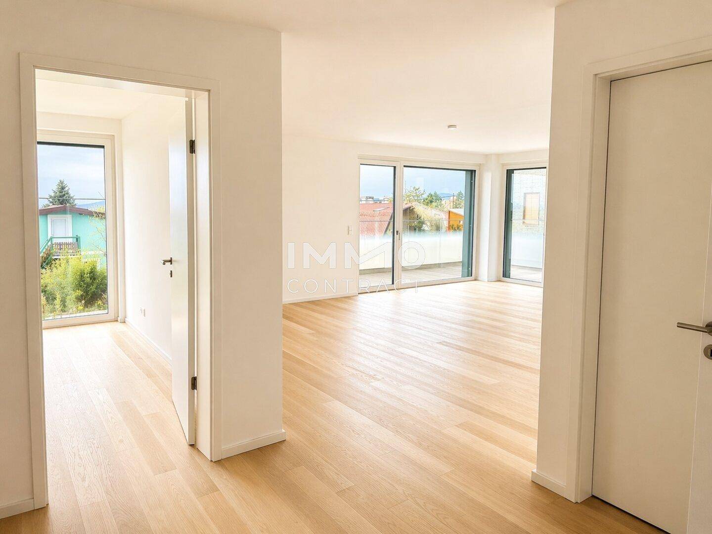 Heller, leerer Wohnbereich mit Holzboden und Zugang zu einer großen Terrasse.