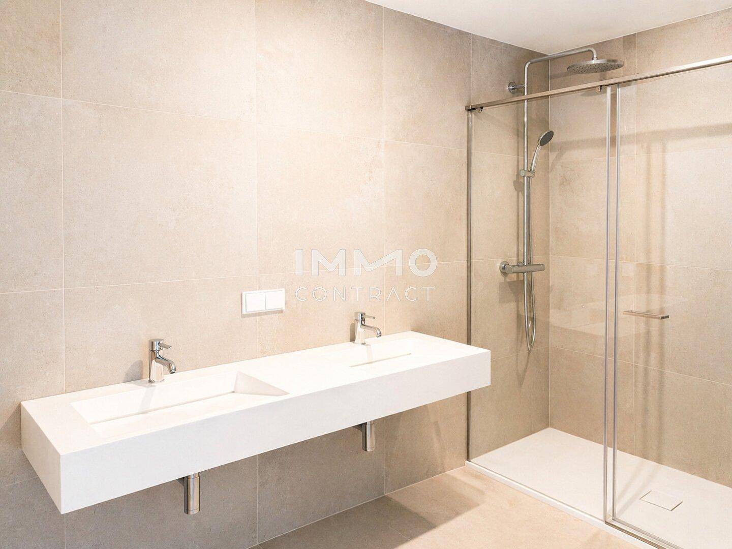 Modernes Badezimmer mit Doppelwaschbecken, großer Dusche und beigefarbenen Fliesen.