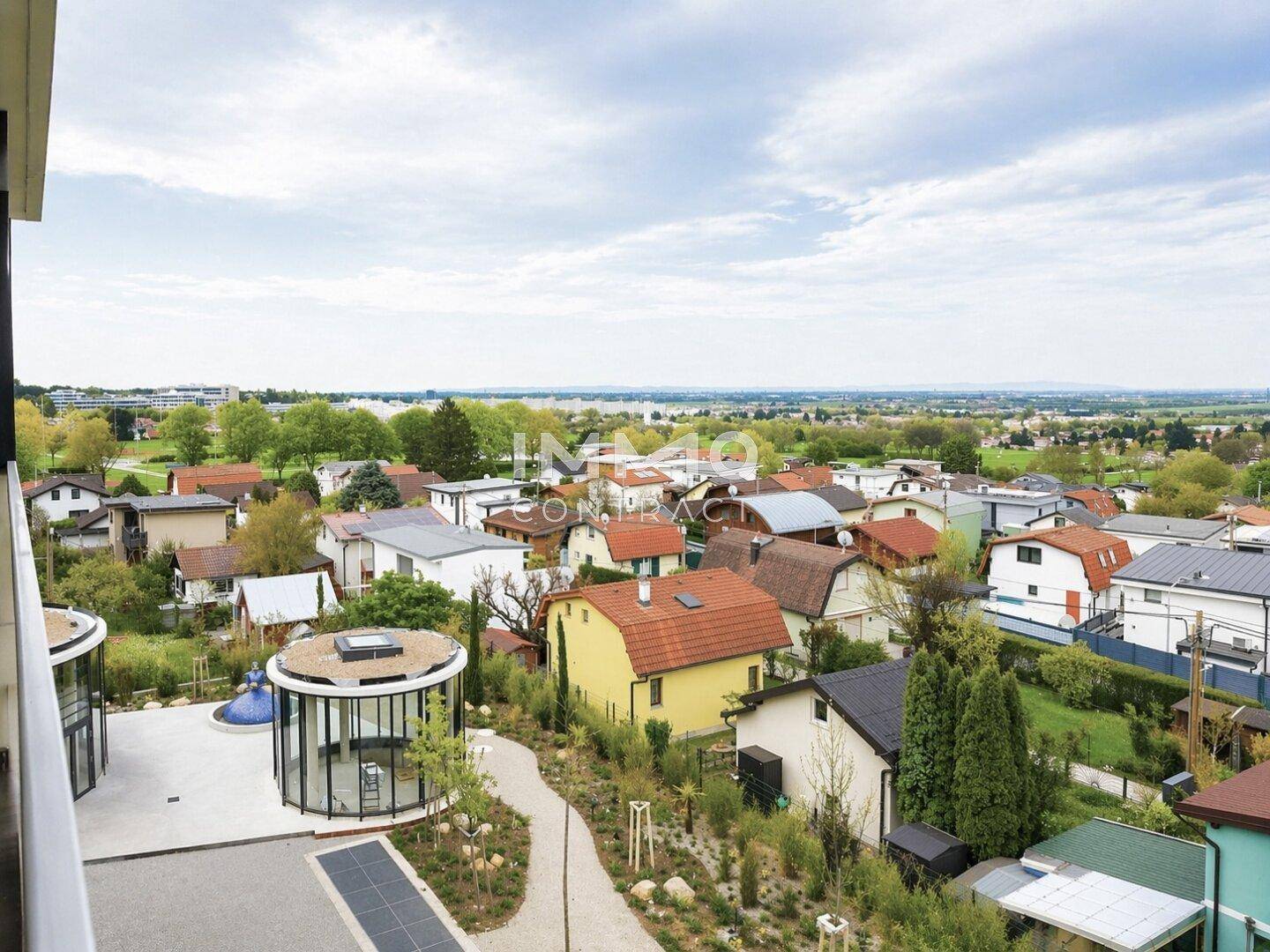 Panoramablick über eine Wohnsiedlung mit grünen Gärten und einem See im Hintergrund.