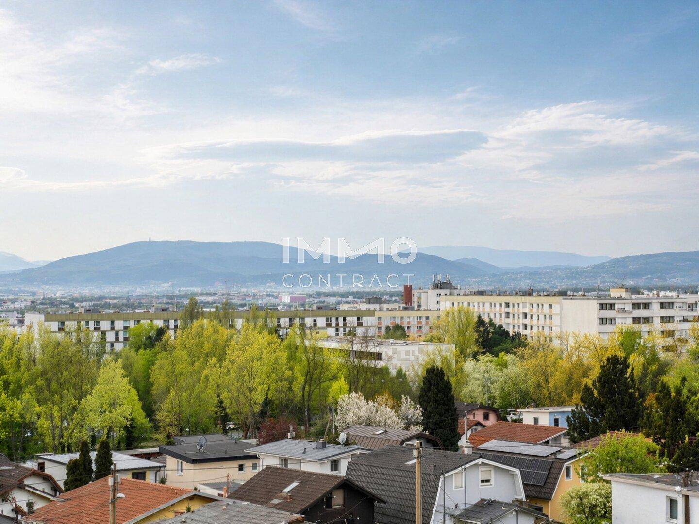 Weitläufiger Blick über die Stadt und grüne Hügel mit Bergen im Hintergrund.