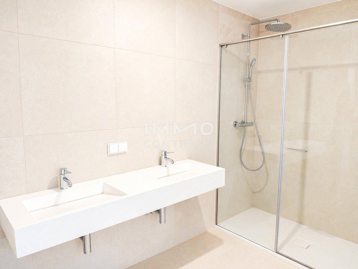 Modernes Badezimmer mit Doppelwaschbecken, großer Duschkabine und hellen Fliesen.