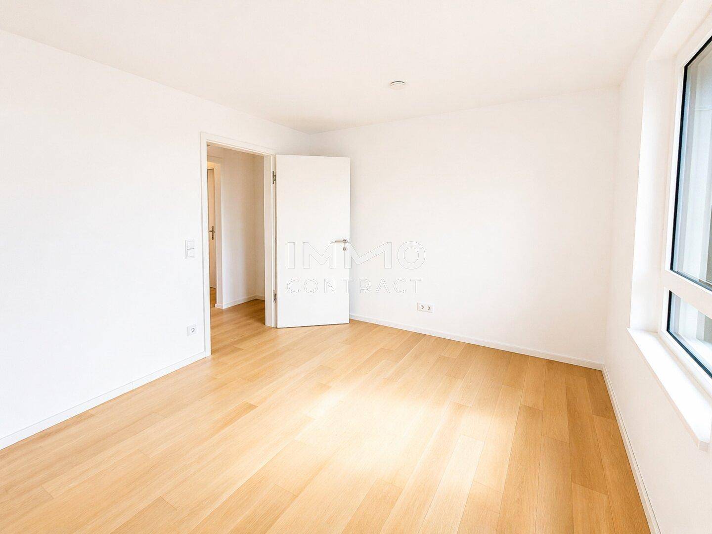 Helles Schlafzimmer mit Parkettboden und einem Fenster, das viel Tageslicht hereinlässt.