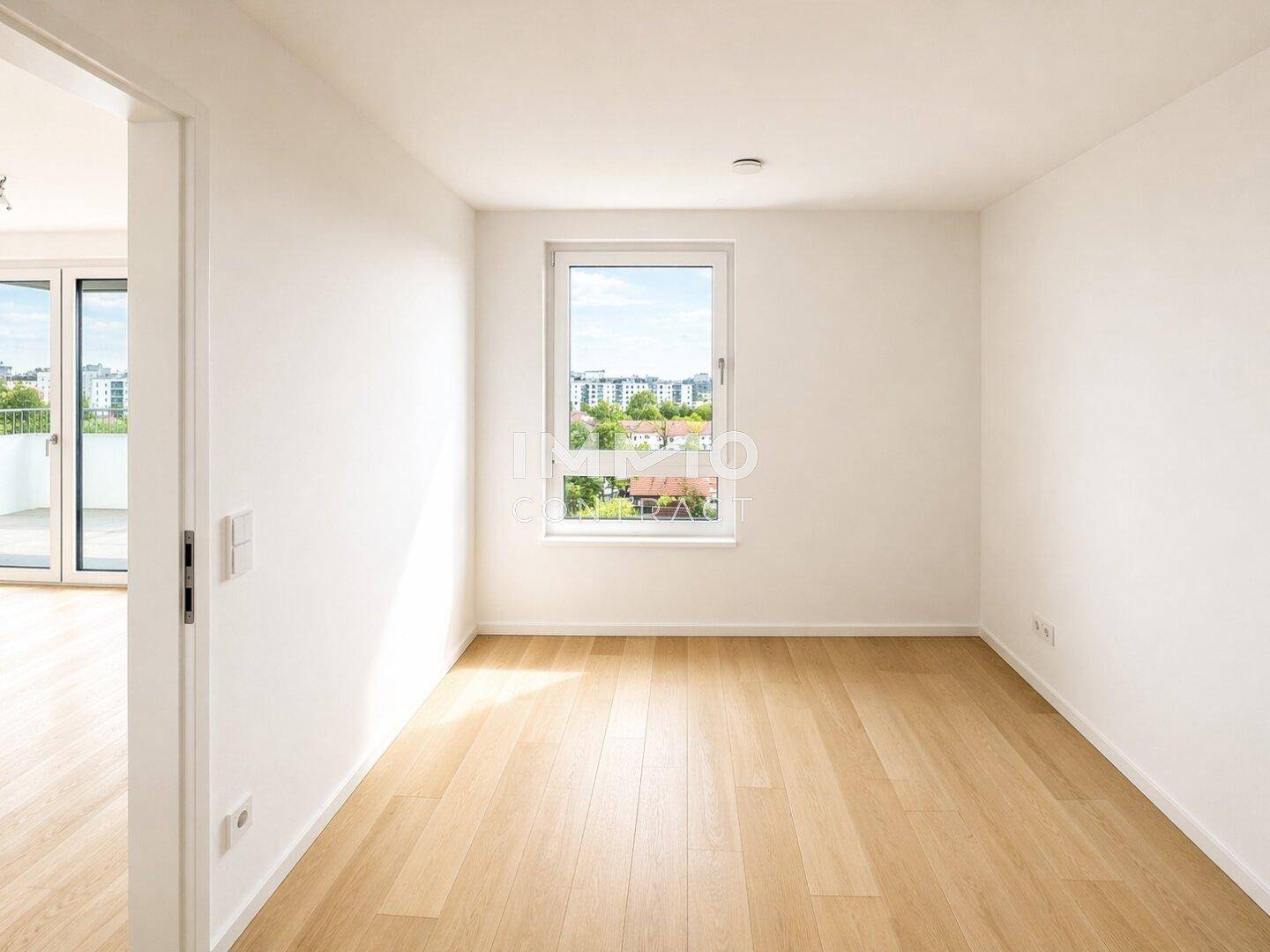 Helles Zimmer mit Parkettboden und einem großen Fenster, das den Blick ins Grüne freigibt.