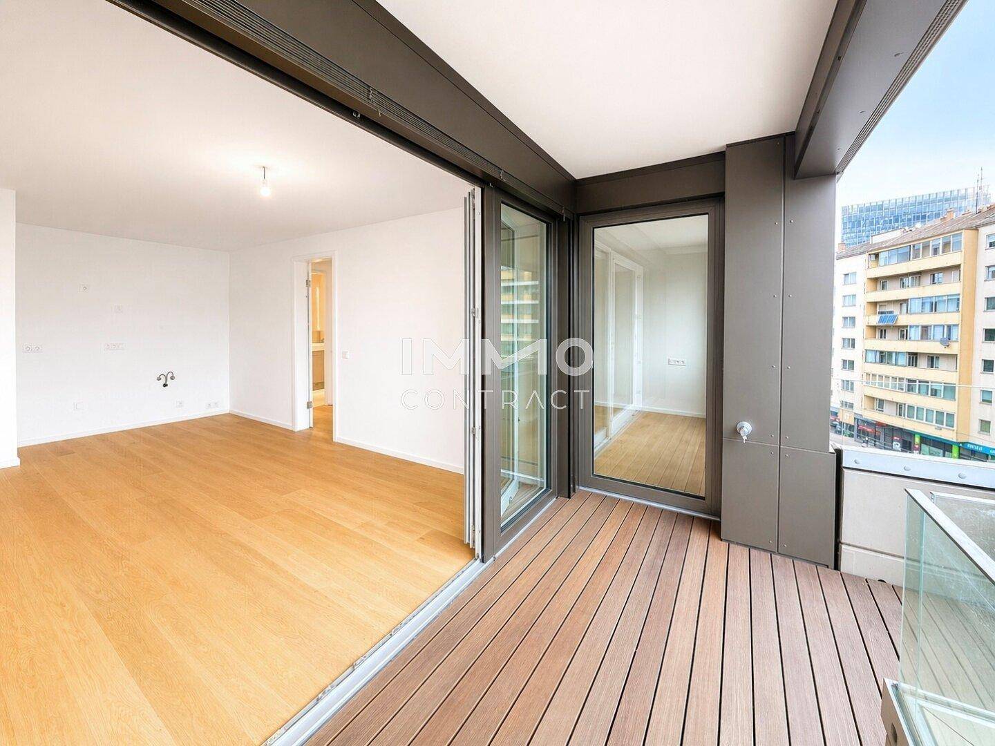 Moderner Balkon mit Holzdielenboden und Glasgeländer, bietet Blick auf die Stadt.