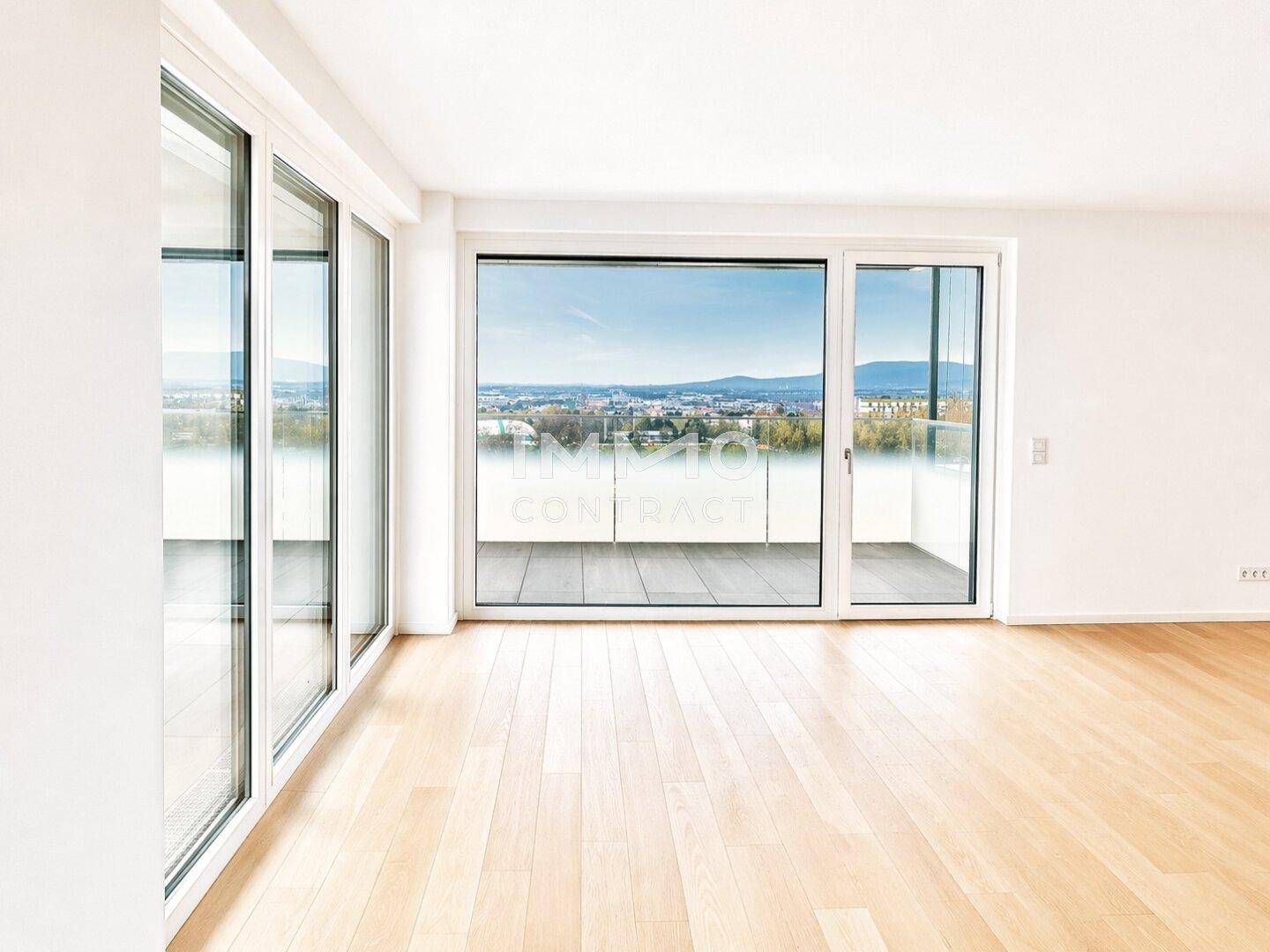 Heller, leerer Raum mit großen Fenstern und Zugang zu einem Balkon mit Panoramablick.