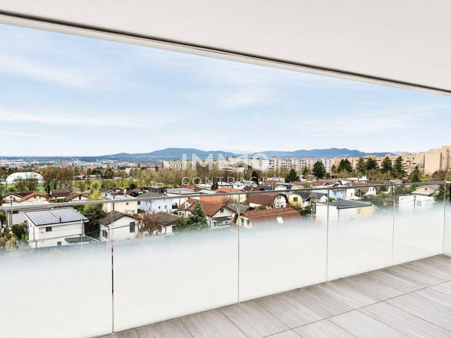 Weitläufiger Ausblick vom Balkon über die Stadt und die umliegende Landschaft mit Bergen im Hintergrund.