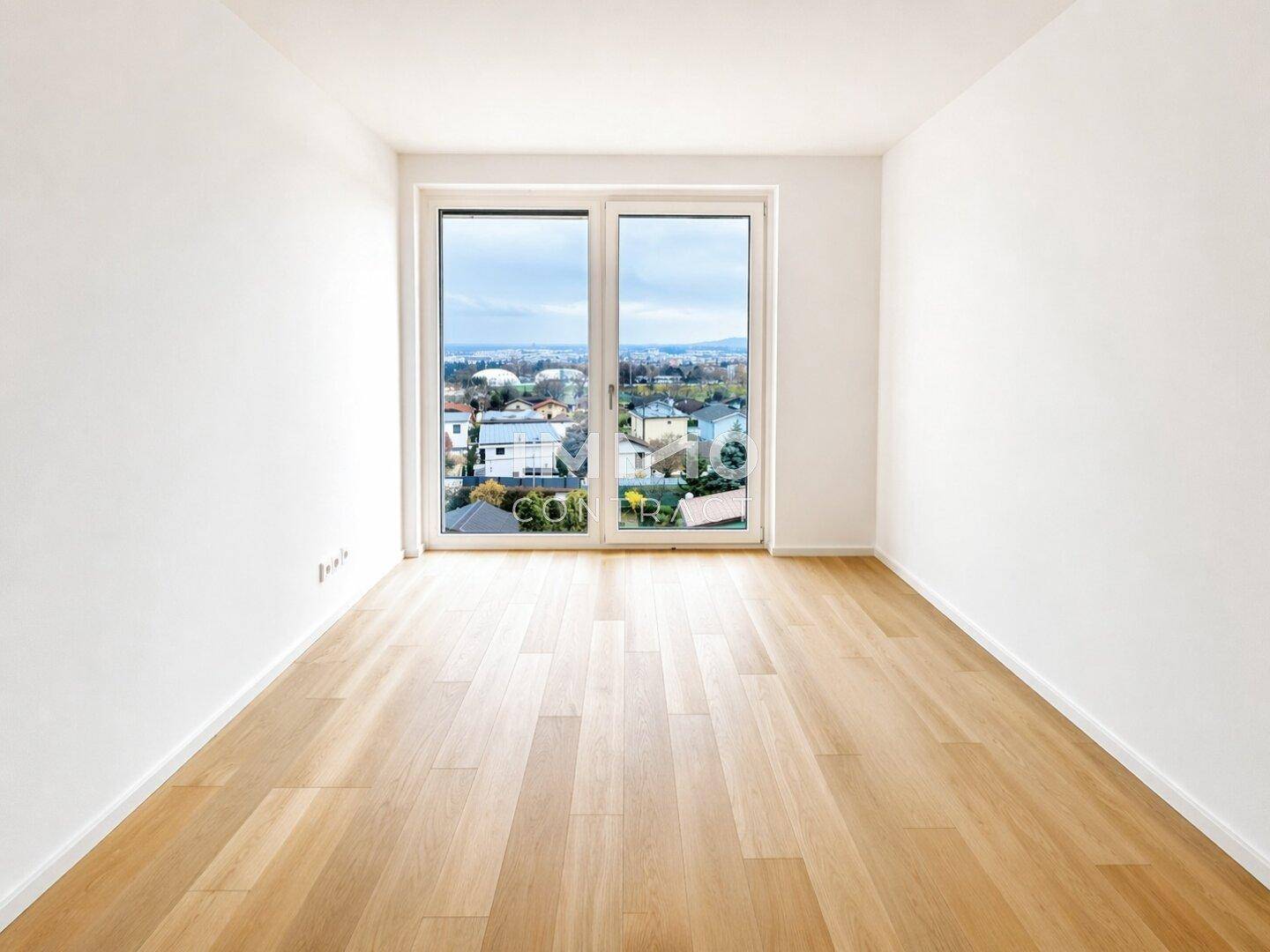 Heller, leerer Raum mit großem Fenster und Holzboden, bietet einen weiten Blick nach draußen.