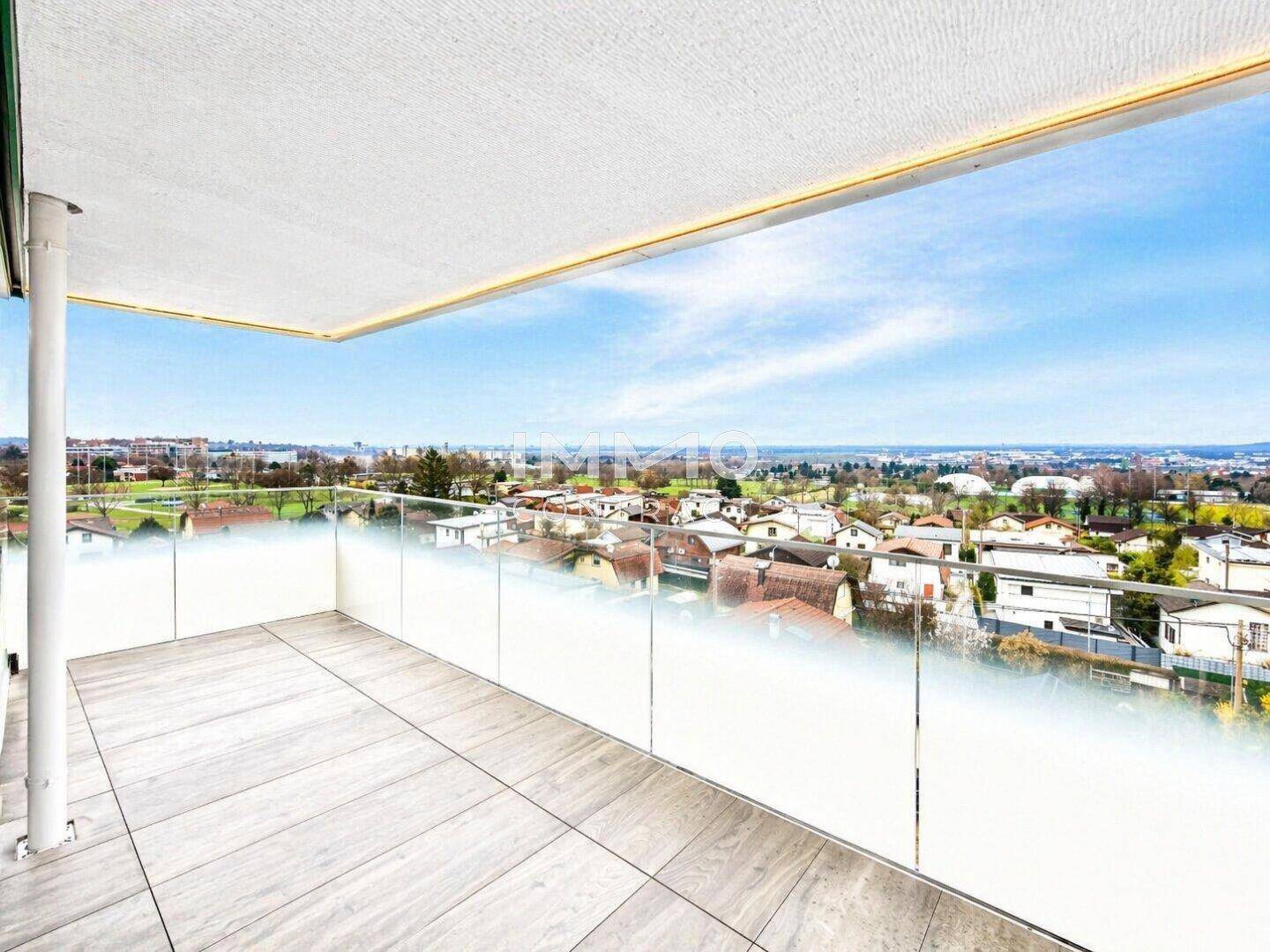 Großer Balkon mit Fliesenboden und Glasgeländer, bietet einen weiten Blick über die Stadt und die Umgebung.